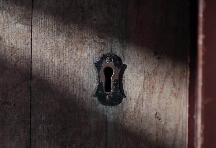 A brief flame flickers and dies in a rusty keyhole on an old wooden door as sunlight fades to complete darkness