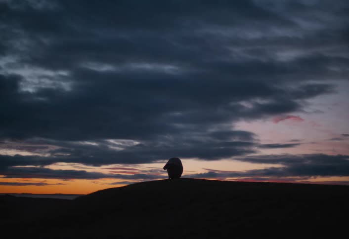 A single sheep walks along a silhouetted ridgeline as the last light of day fades on the horizon