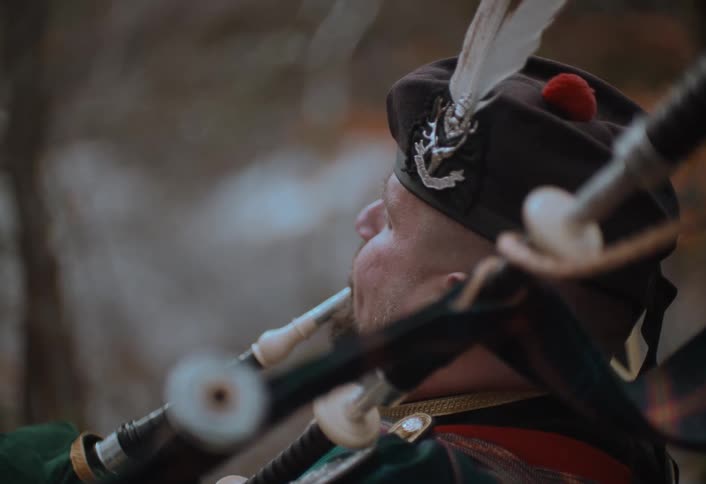 A cinematic close-up profile of a man in traditional Scottish attire playing the bagpipes in a moody forest setting