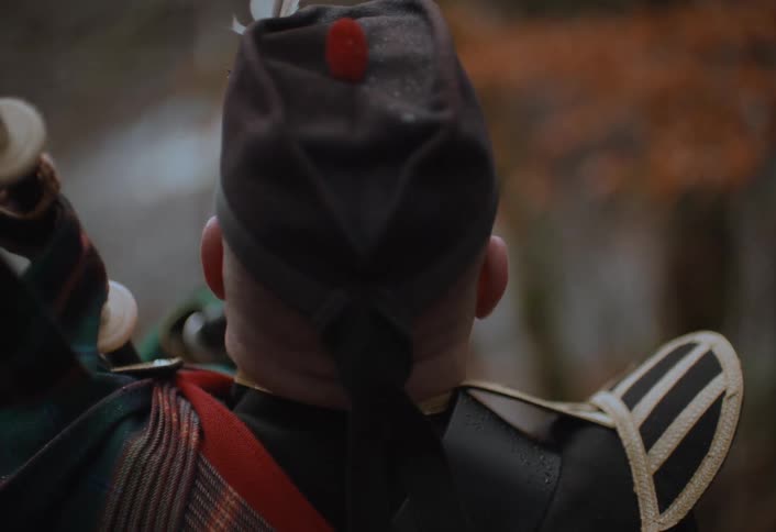 A cinematic over-the-shoulder slow-motion shot of a man playing the Scottish bagpipes in traditional garb