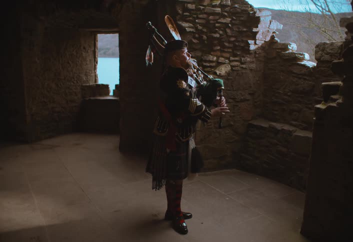 A Scottish bagpiper in a traditional kilt plays a somber tune inside the ancient stone ruins of a castle