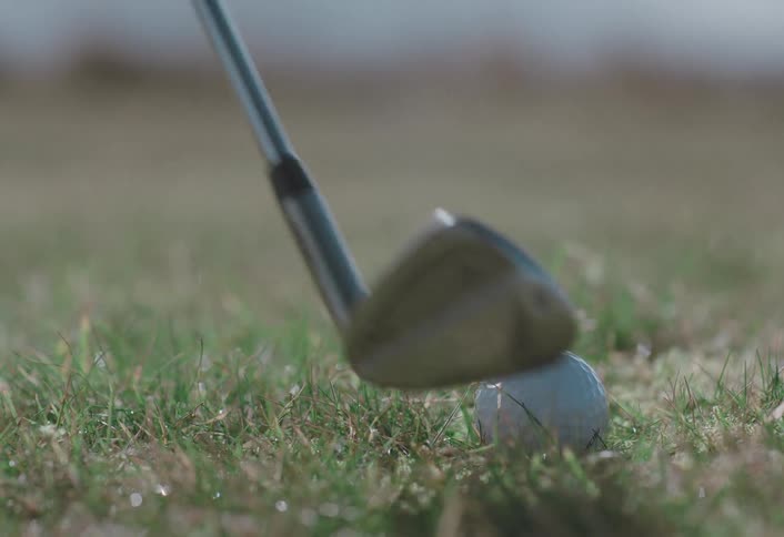 A close-up, slow-motion shot of a golf iron hitting a ball on a dewy fairway