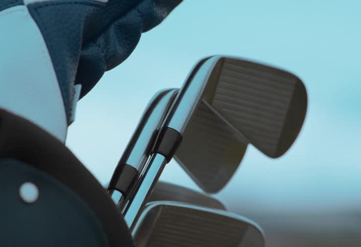 Close up of a golfer's gloved hand selecting a shiny iron from their golf bag