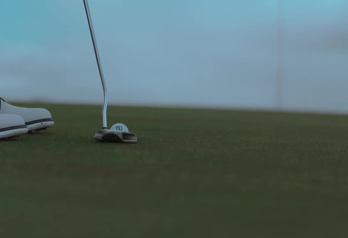 A golfer carefully lines up and executes a putt in a slow-motion close-up on the green