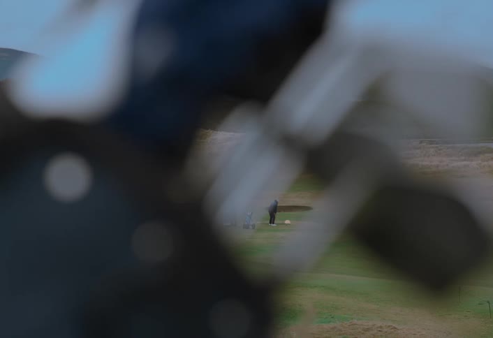 A golfer swings his club on the green as seen from a unique perspective behind a golf bag