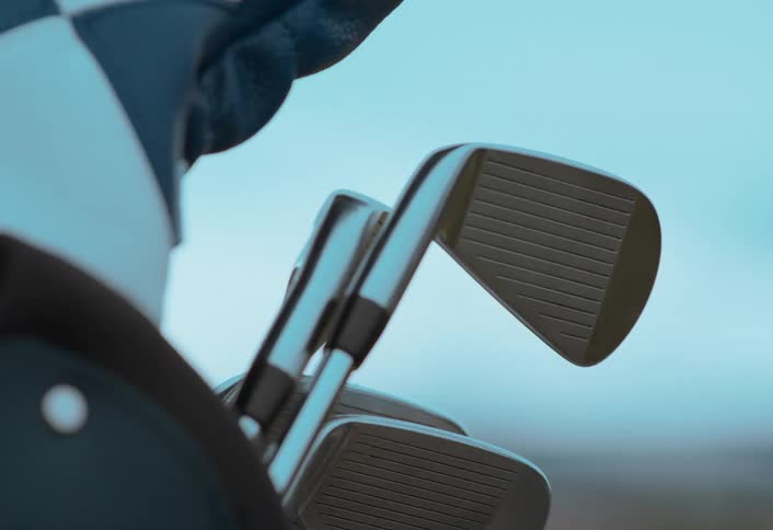 A close-up slow-motion shot of a golfer's gloved hand selecting an iron from a golf bag