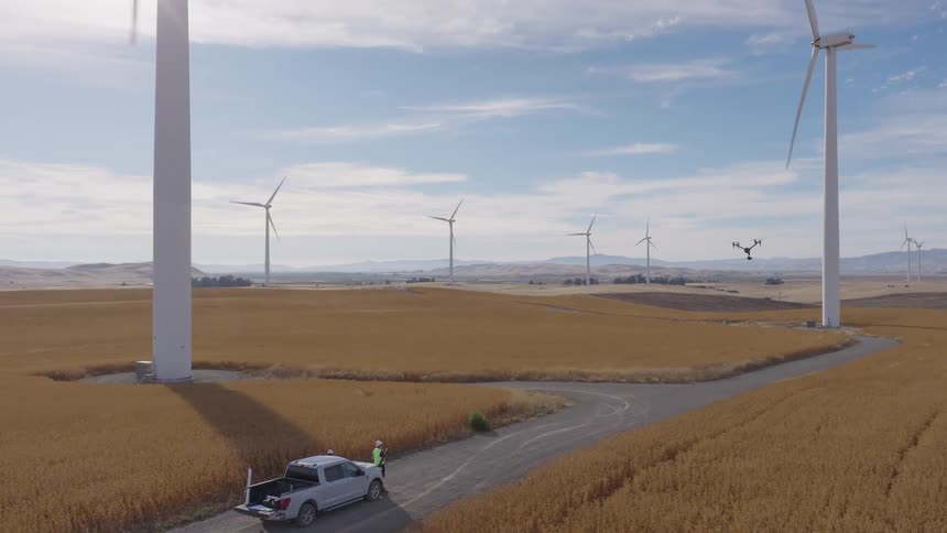 Aerial view of a drone pilot conducting a maintenance inspection of a wind turbine at a vast wind farm