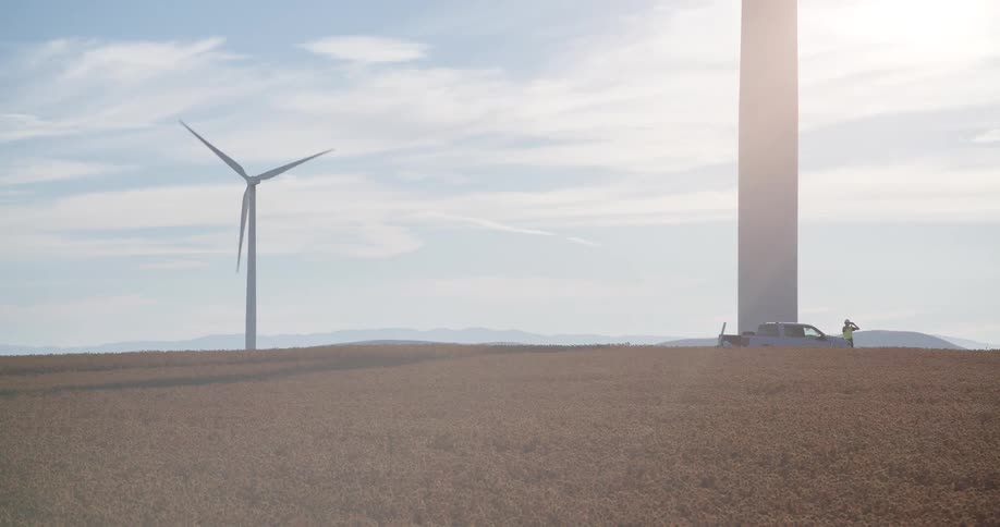 A technician inspects a massive wind turbine on a wind farm located in a sprawling golden field on a sunny day
