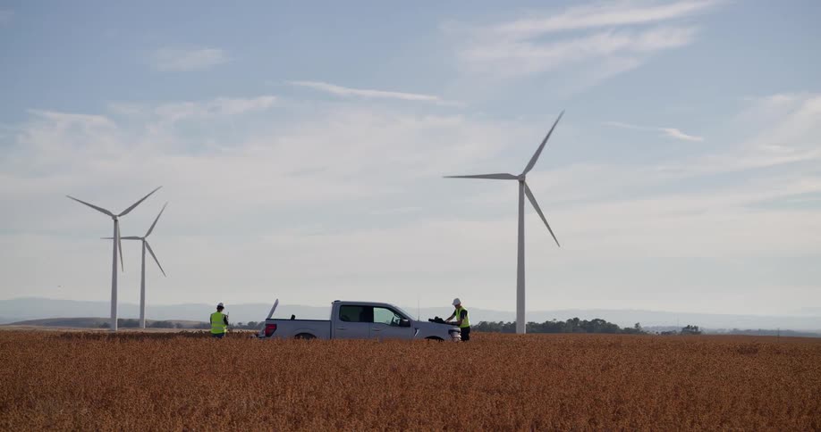 Two engineers conduct a site inspection at a wind farm, standing by their truck in a vast golden field