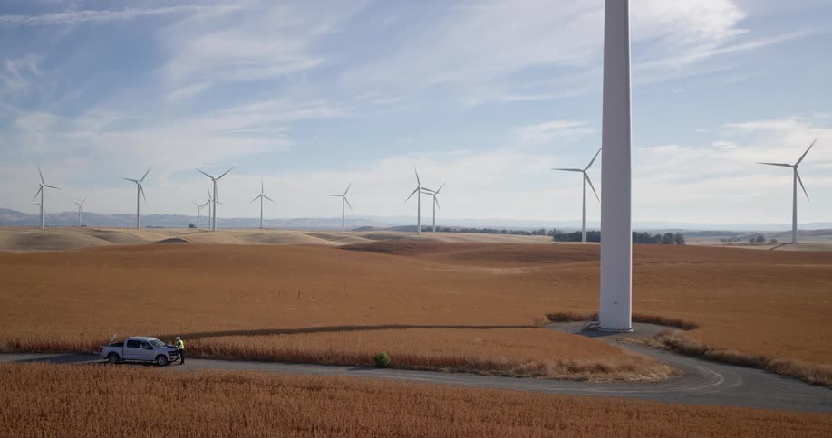 Engineers in safety vests conduct a maintenance check at the base of a towering wind turbine on a vast rural wind farm