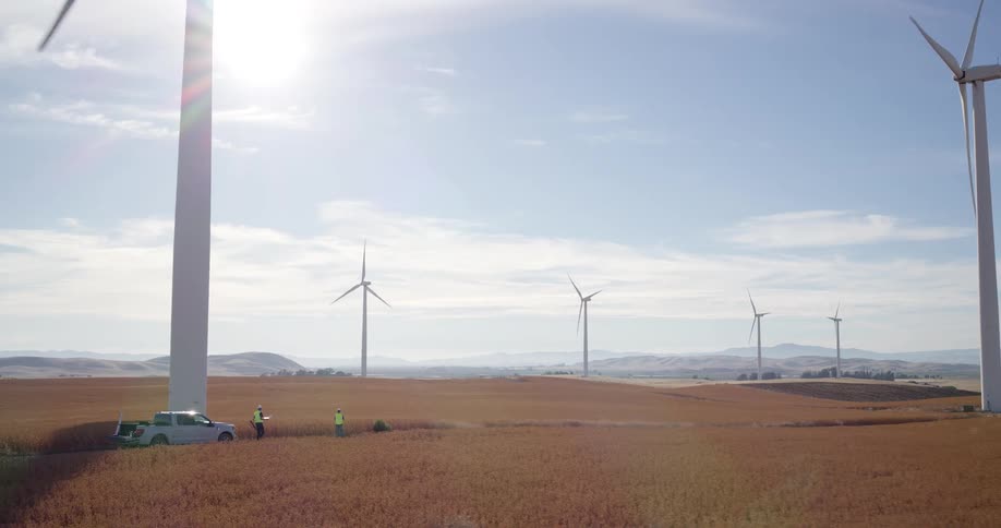 Engineers in safety vests perform a maintenance check at the base of a massive wind turbine on a sunny day