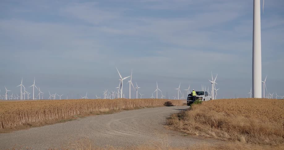 Two engineers survey a massive wind farm from a dirt road in a golden wheat field
