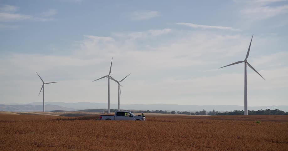 Engineers in a pickup truck perform an inspection at a large wind farm located in a golden field of rolling hills
