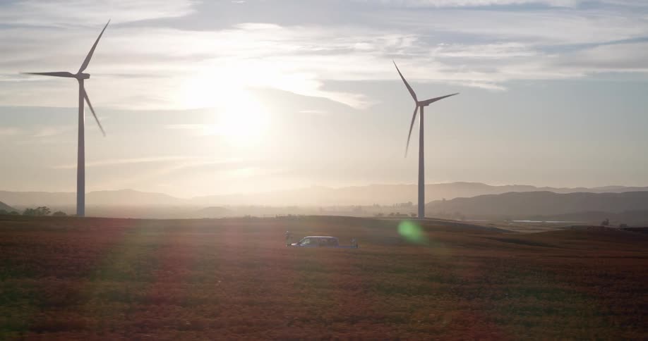 Aerial view of a vast wind farm with spinning turbines in a golden field as the sun sets over distant mountains