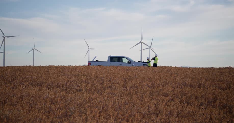 Two engineers discuss plans on the hood of their truck in a field of a wind farm
