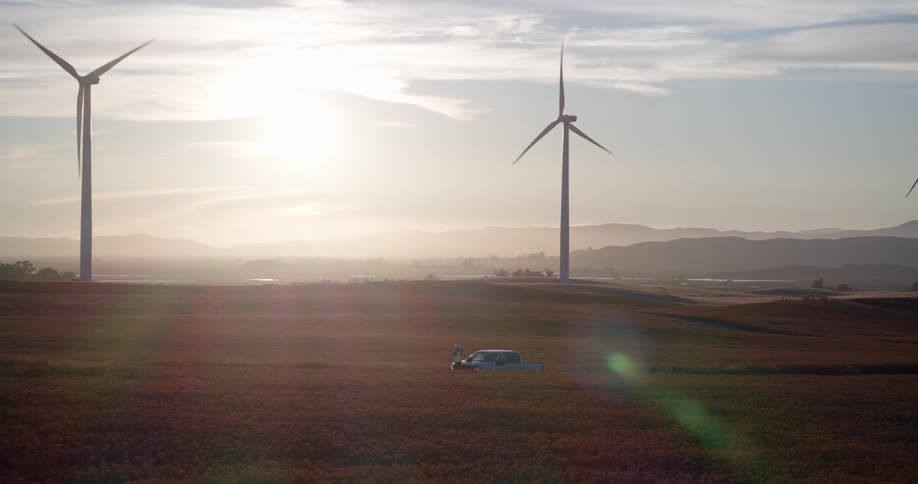 A futuristic eVTOL aircraft takes off from a vast field at sunrise, flying across a landscape dotted with spinning wind turbines