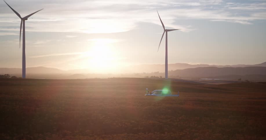 A beautiful aerial view of a wind farm technician standing by their truck in a golden field as the sun rises