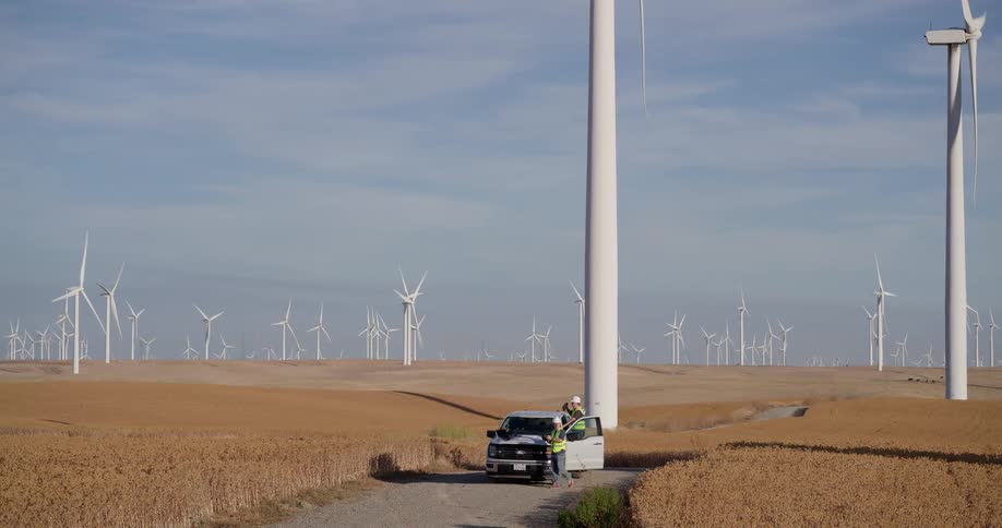 Two wind turbine technicians in safety gear review plans on their work truck at a vast renewable energy farm