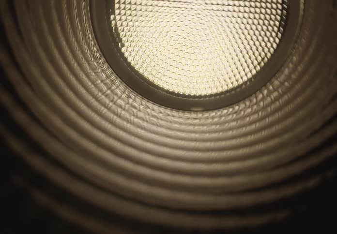An abstract dolly shot pushes through a dark, ribbed tunnel towards a bright light at the end
