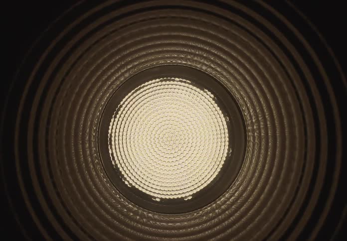 A slow, hypnotic zoom through a dark, ribbed circular tunnel towards a bright light source