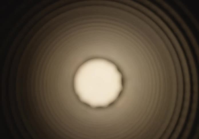 Abstract backward dolly shot revealing the interior of a dark, corrugated industrial pipe with a bright light at the end