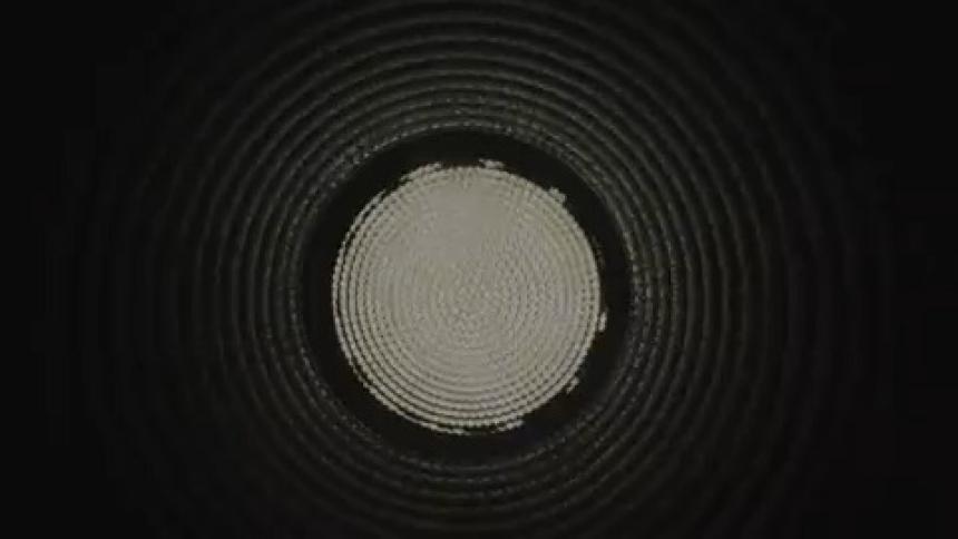 A hypnotic, pulsating circular light strobes at the end of a dark, corrugated industrial tunnel