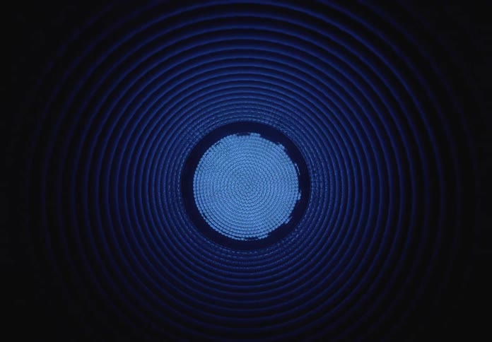 A colorful, glowing LED light pulsates at the end of a dark, abstract, ribbed tunnel
