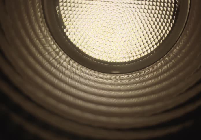 Abstract macro shot moving slowly through a circular, corrugated tube towards a bright light at the end