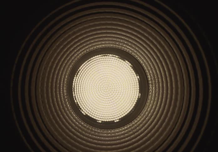 A hypnotic view looking down a dark, corrugated industrial tube towards a bright circular LED light at the end