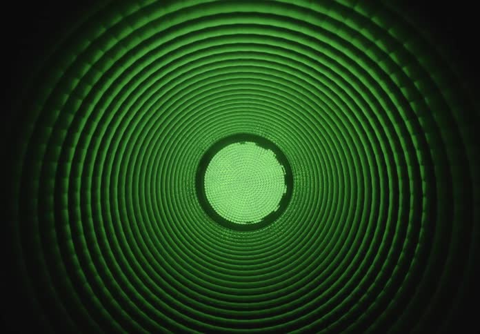 A hypnotic view inside a ribbed tunnel where green, red, and blue lights pulse and fade in the darkness