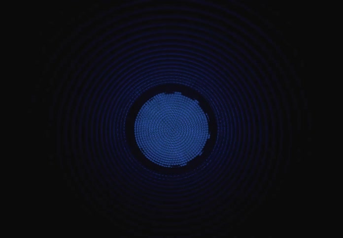 A hypnotic view inside a ribbed tunnel where green, red, and blue lights pulse and fade in the darkness