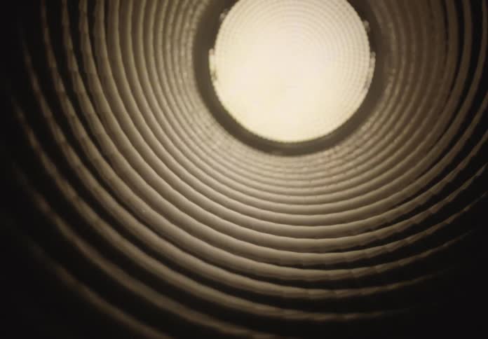 A slow, hypnotic journey through a dark corrugated pipe toward a bright, textured light at the end of the tunnel
