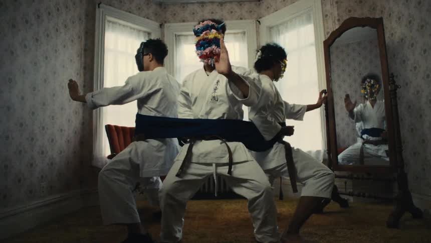 A bizarre montage cuts from the feet of a person in a bathroom stall to three masked martial artists tied together in a vintage room