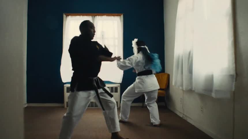 A male and female black belt practice synchronized karate moves together outdoors in a park and indoors in a dojo