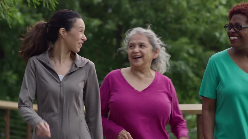 Slow motion shot of three female friends of varying ages laughing together during their morning walk in the park