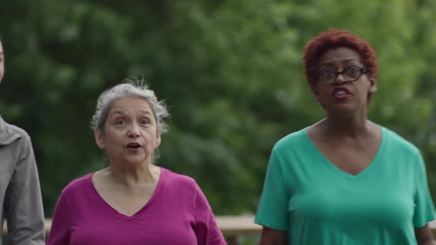 A diverse group of three women laugh and talk while enjoying a power walk together outdoors in slow motion