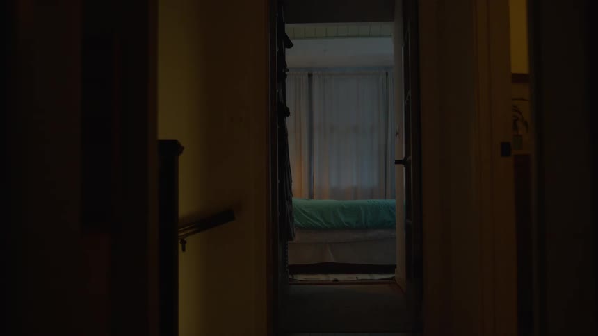 A woman walks through a dark house into her bedroom, lights a candle, and gets into bed to go to sleep