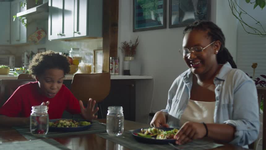 A happy mother serves a healthy home-cooked meal to her excited son at the dining table in slow motion