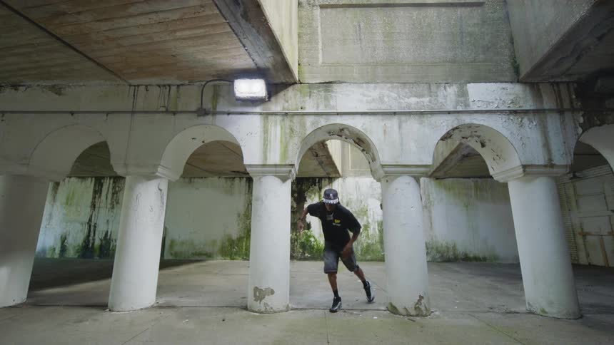 A skilled street dancer performs an energetic hip-hop routine in a gritty urban underpass surrounded by weathered white pillars