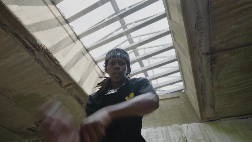 Energetic young Black man dances intensely towards the camera in a slow-motion, low-angle shot inside a gritty industrial space