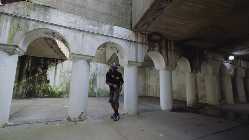 A talented street dancer performs an expressive routine in slow motion within a gritty urban underpass featuring white pillars