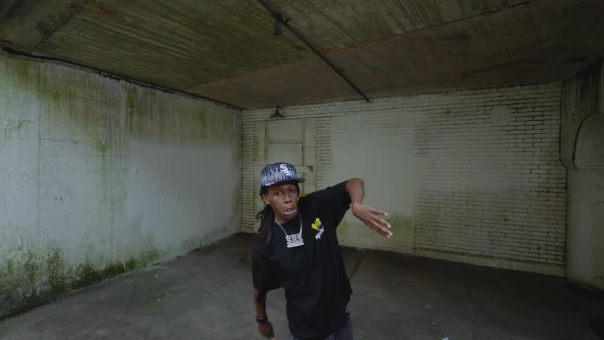 A stylish young man with dreadlocks performs a dynamic dance routine in slow motion inside an old, empty garage