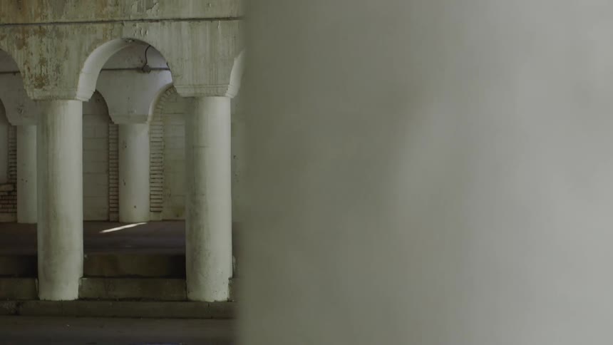 A young man with dreadlocks slowly walks past the white columns of a gritty, boarded-up urban walkway