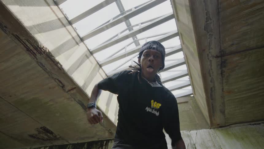 Energetic male krump dancer performs powerful moves in slow motion under a large skylight in a gritty, industrial setting
