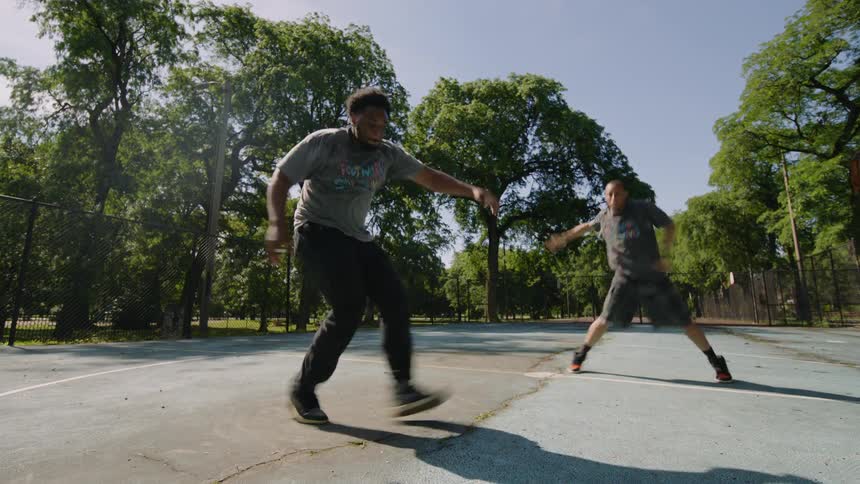 Two talented dancers perform a synchronized footwork routine on an outdoor court in a sunny urban park