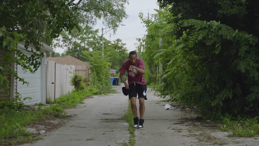 A talented young man performs an expressive street dance routine in slow motion down a gritty, overgrown urban alley