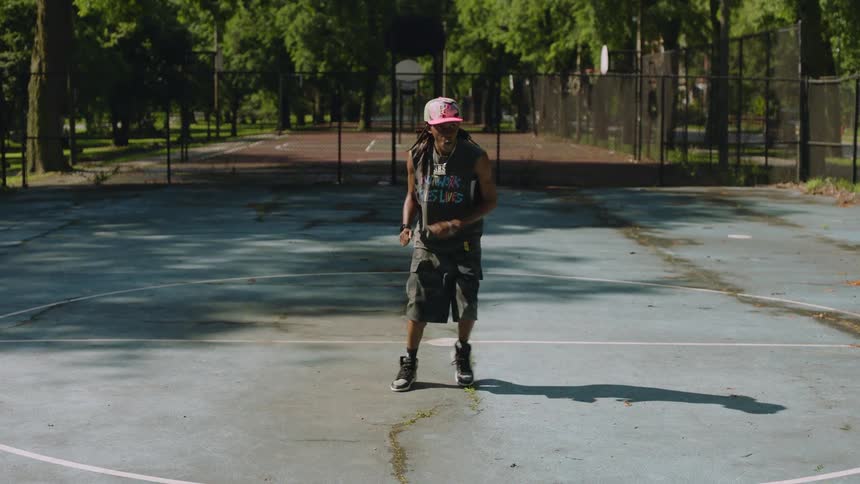 A talented man performs intricate hip-hop footwork in slow motion on a sunny outdoor basketball court