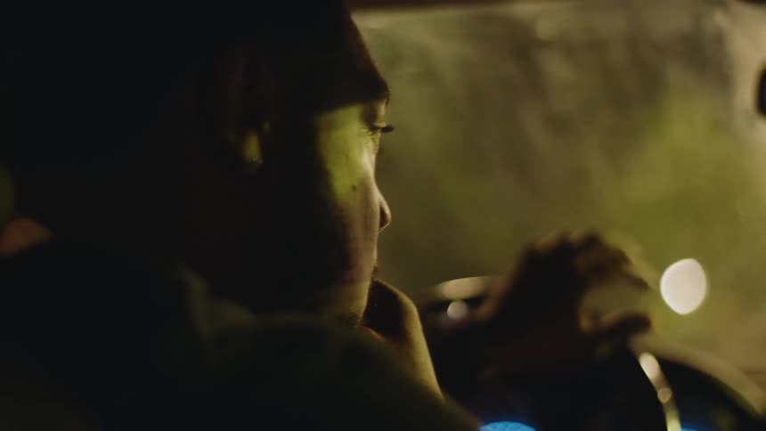 Close-up of a man vaping and smoking while driving a car at night in slow motion