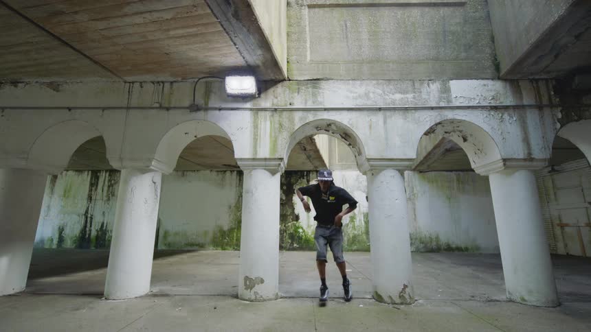 A young man performs an expressive slow motion dance routine in a gritty urban structure with white pillars and arches