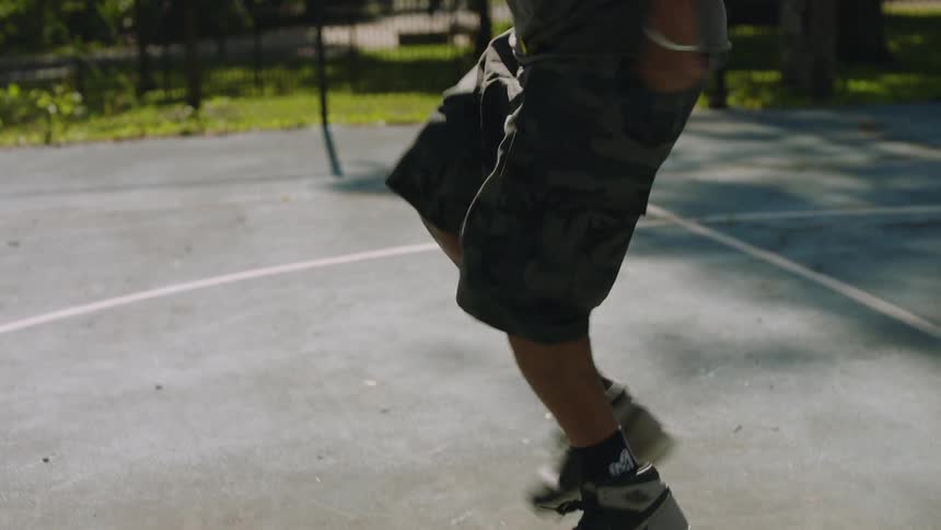 A skilled footwork dancer showcases incredible moves in slow motion on a sunny day at a park basketball court